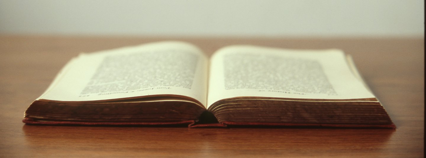 Un libro aperto e invecchiato giace su un tavolo di legno lucido.